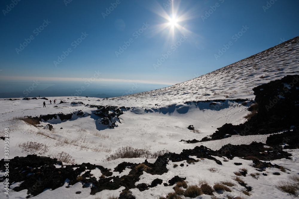 group of hikers walk on the snow in a sunny day, with blue sky and sea in background on a path of Mount Etna. Etna National Park, Catania, Sicily, Italy