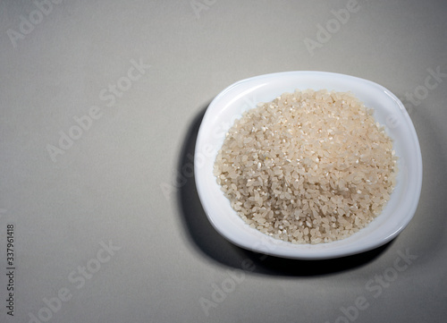Raw rice on a white plate on the background. Ingredient for cooking. View from above.