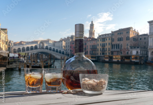 Drink for two in Venice - two glasses of lying liqueur and a bottle - panorama of the city of Venice with Rialto bridge