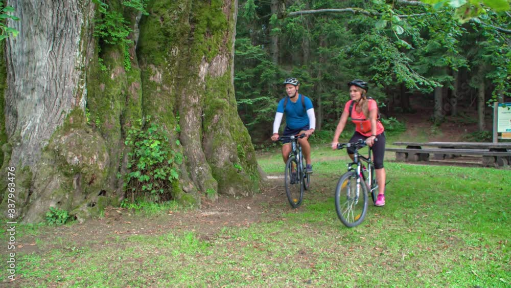 Active couple riding on bicycles in the forest near a famous Najevska Linder Tree in Slovenia. Active couple riding on bicycles in the forest near a famous Najevska Linder Tree in Slovenia.