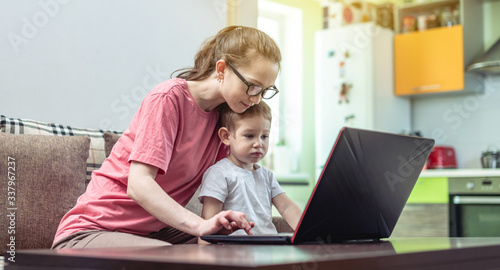 Woman with a small child on her knees is sitting at a laptop. Remote work and receiving online education of home