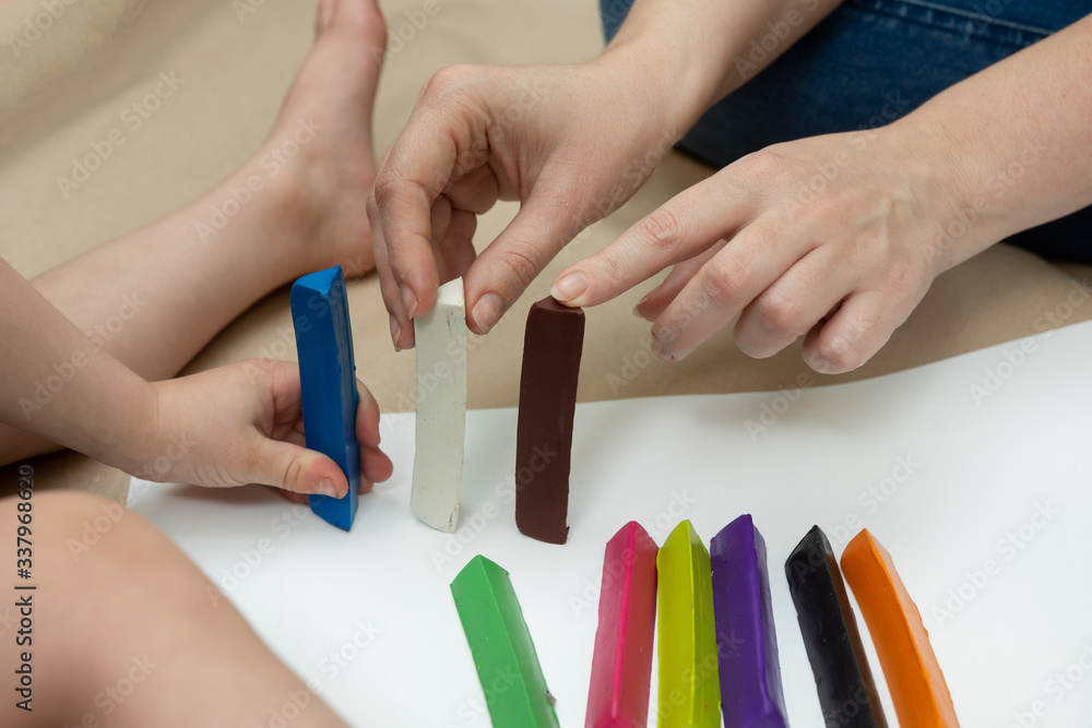 Fototapeta premium a little boy with his mother are building a multi-colored fence from plasticine bars. family leisure. close-up