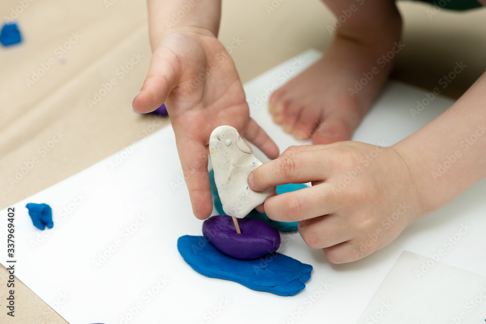 a small child sculpts a sailboat from plasticine. self-isolation classes a small child sculpts a sailboat from plasticine. self-isolation classes