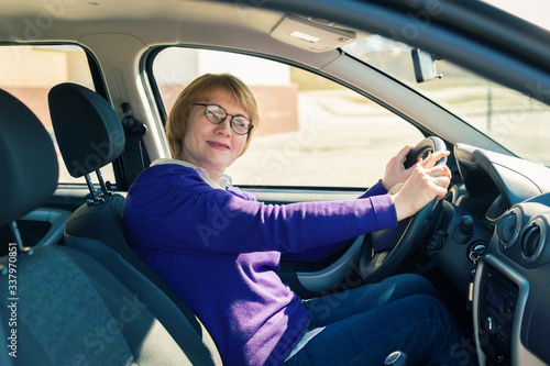 A woman sits in a car behind the wheel and looks at the road