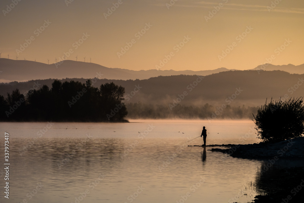 Lonely fisherman angling at a lake in the early morning just after sunrise, Ullibarri-Gamboa Reservoir, Alava, Basque Country, Spain