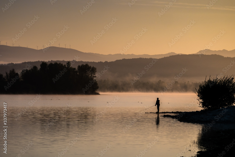 Lonely fisherman angling at a lake in the early morning just after sunrise, Ullibarri-Gamboa Reservoir, Alava, Basque Country, Spain Lonely fisherman angling at a lake in the early morning just after sunrise, Ullibarri-Gamboa Reservoir, Alava, Basque Country, Spain