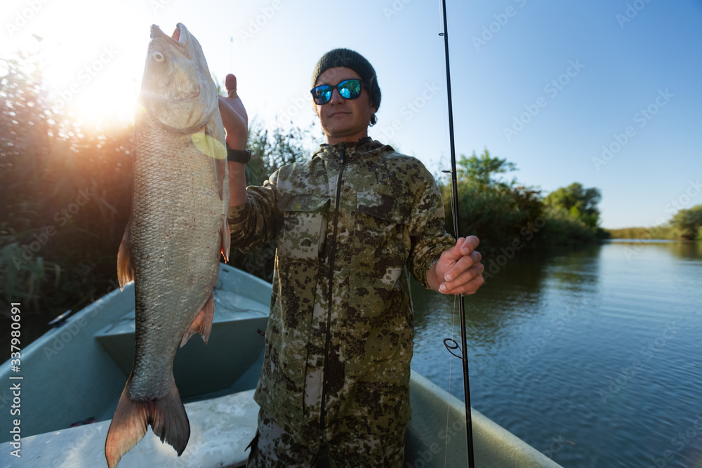 Fisherman holds Asp fish standing in the boat on the river Fisherman holds Asp fish standing in the boat on the river