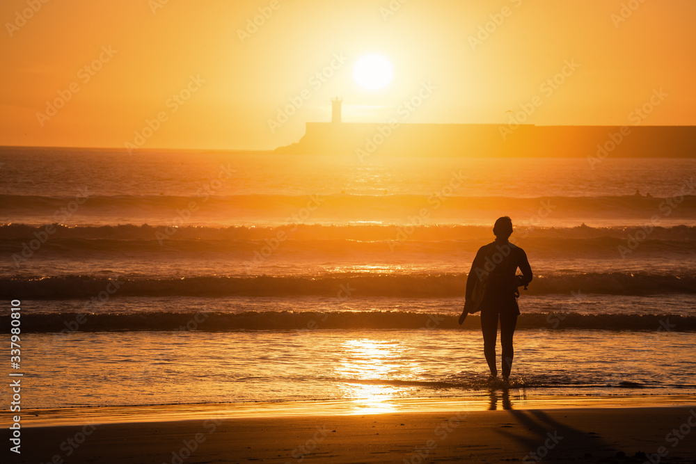 Silhouette of male surfer coming from a ocean waves,Sunset light, unrecognizable person, lens flare, copy space.