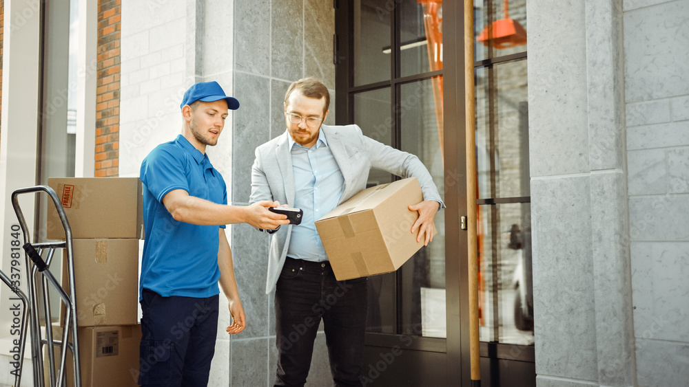 Delivery Man Gives Postal Package to a Business Customer, Who Signs Electronic Signature POD Device. In Stylish Modern Urban Office Area Courier Delivers Cardboard Box Parcel to a Man Delivery Man Gives Postal Package to a Business Customer, Who Signs Electronic Signature POD Device. In Stylish Modern Urban Office Area Courier Delivers Cardboard Box Parcel to a Man