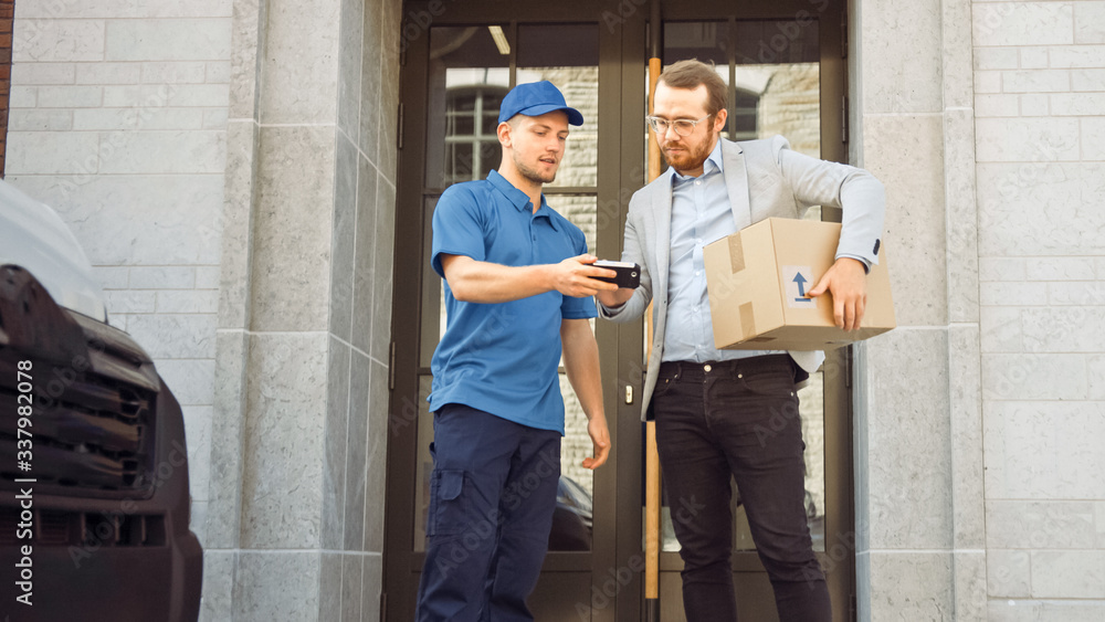 Delivery Man Gives Postal Package to a Business Customer, Who Signs Electronic Signature POD Device. In Stylish Modern Urban Office Area Courier Delivers Cardboard Box Parcel to a Man Delivery Man Gives Postal Package to a Business Customer, Who Signs Electronic Signature POD Device. In Stylish Modern Urban Office Area Courier Delivers Cardboard Box Parcel to a Man