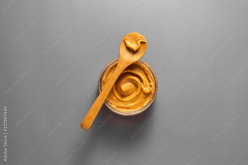Peanut butter jar with wooden spoon over grey background with copy space.