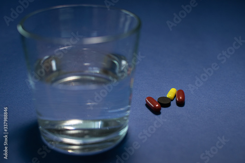 Medical capsules, pills, vitamins and glass of water on a blue background. Drink a pill of water. Drugstore, illness, pain, quarantine, treatment. medicines in the package and poured on the table