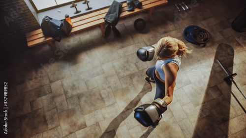 Professional Female Fighter Exercises Kicking and Punching Air while Wearing Sportswear and Fighting Gloves in the Hardcore Gym. Strong Beautiful Girl Kickboxing and Self Defense Workout. Top View