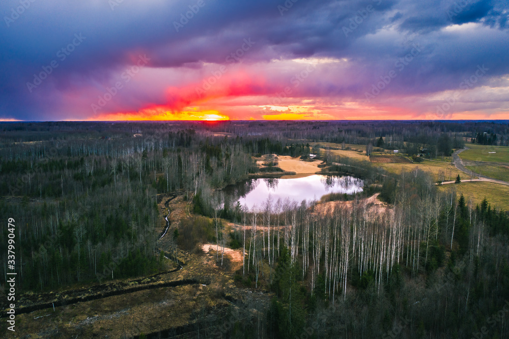 Aerial view over forest with dark storm clouds. Lake in the forest at colorful twilight. 
