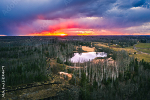 Aerial view over forest with dark storm clouds. Lake in the forest at colorful twilight. 