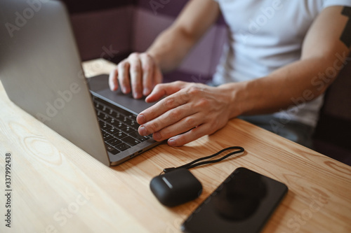 Unrecognizable man hands with smartphone and headphones working on a laptop during coronavirus isolation home quarantine. Covid-19 pandemic Corona virus. Distance online work from home concept.