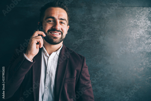 Portrait  caucasian businessman in formal wear having mobile phone conversation, handsome prosperous millennial male talking on smartphone indoors standing near wall satisfied with connection.