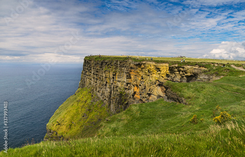 View of the Cliffs of Moher on the Irish coast with blue sky and white clouds.