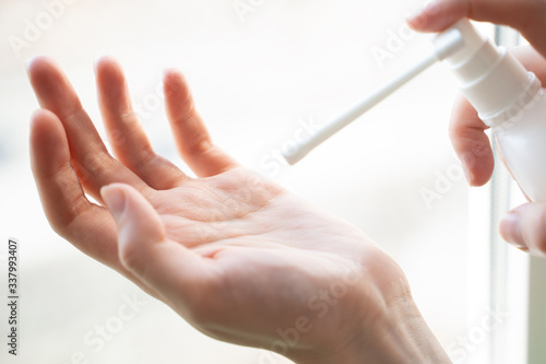 Close up of a woman   s hands applying alcohol hand sanitizer from a small transparent bottle
