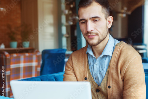A young man works behind a laptop in a cozy cafe. Business and coworking concept. Portrait of a man.