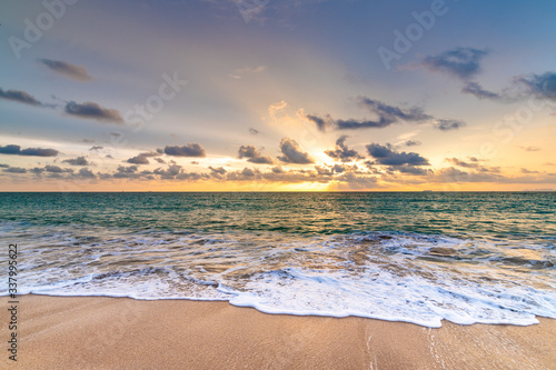 Fototapeta Naklejka Na Ścianę i Meble -  Beautiful sunset above sea or ocean. Vibrant and soft colors, magic light. Small clouds on the sky, reflection of sun in the water and sand on beach. Concept of romantic time on vacation in tropical.