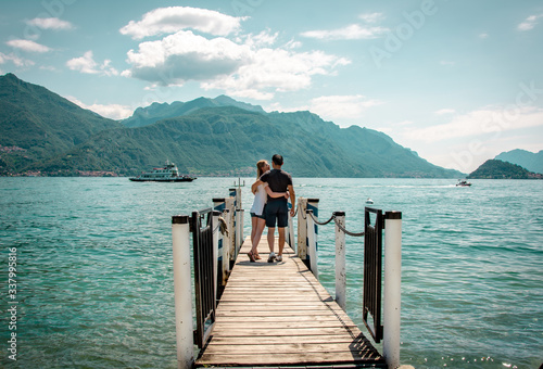Junges Paar am Steg genießt Arm in Arm die Aussicht am Comer See in Italien