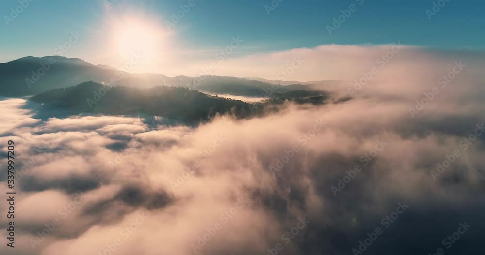 Flying over the clouds during morning sunrise in Carpathian Mountains, Ukraine.golden fluffy clouds moving softly on the sky and the sun shining through the clouds with beautiful rays and lens flare.
