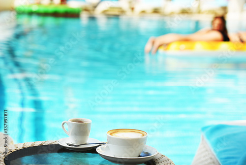 A cup of coffee and cappuccino on a pool table. A cozy place to relax by the pool. summer sunny day.
