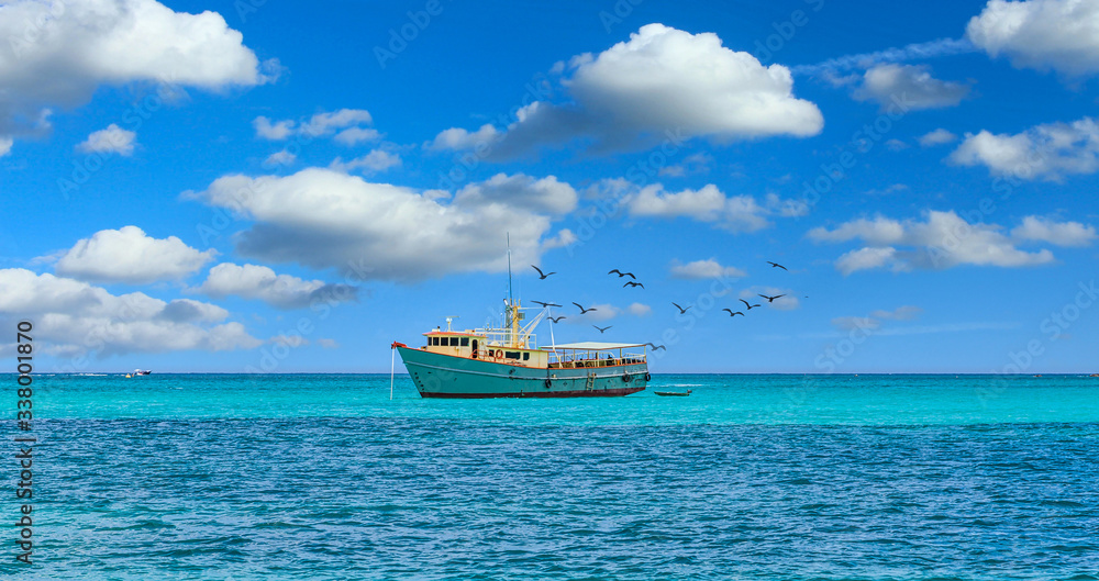 An old yellow and white fishing boat moored on aqua Caribbean water