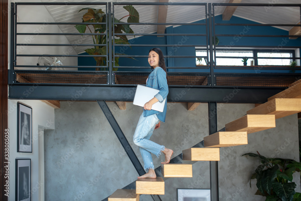 Young woman going downstairs, holding laptop under arm, smiling Young woman going downstairs, holding laptop under arm, smiling