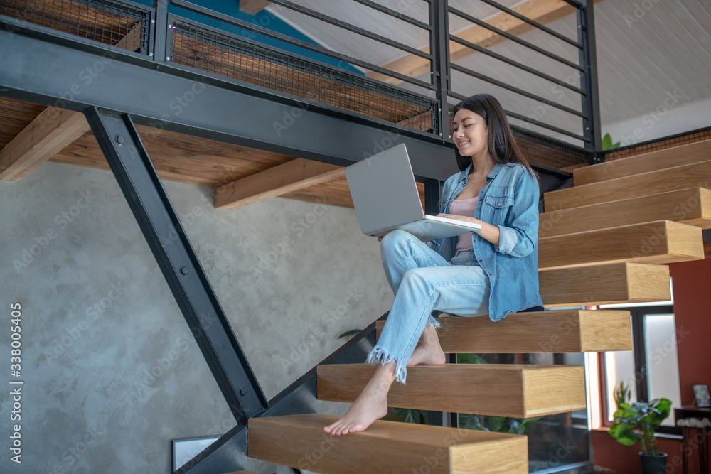 Young woman sitting on stairs, holding laptop on knees, typing