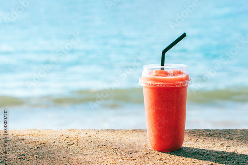 Closeup glass of strawberry smoothie with lignt in the morning and sea water background, Holiday and relax time