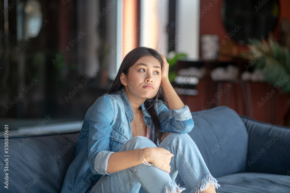 Sad young woman sitting on sofa, resting her head on her hand Sad young woman sitting on sofa, resting her head on her hand
