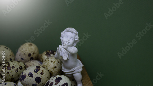 Еaster background. Delicate white angel on a green background with small eggs.