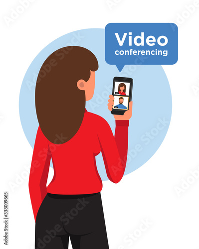 Close-up of a stand up woman from behind communicating by video conference with a man. Virtual meeting. Video conference. Video chat. Plain background.
