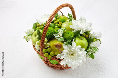 Wicker basket filled with fruits, white and green flowers on a white background