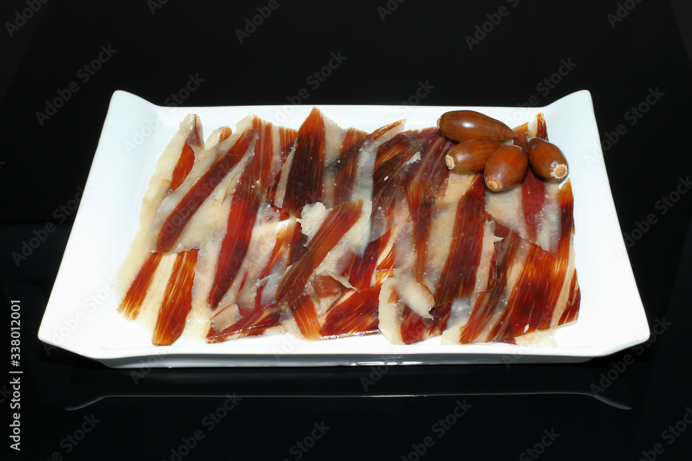 Iberian ham dish with acorns on black background