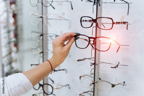 Row of glasses at an opticians. Eyeglasses shop. Stand with glasses in the store of optics. Woman's hand chooses spectacles. Eyesight correction. © Vadim