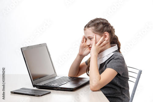 Cute schoolgirl sitting at a laptop on a white background