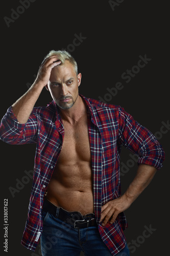 Sexy young handsome naked man,  wears plaid shirt  stands thinking on dark background