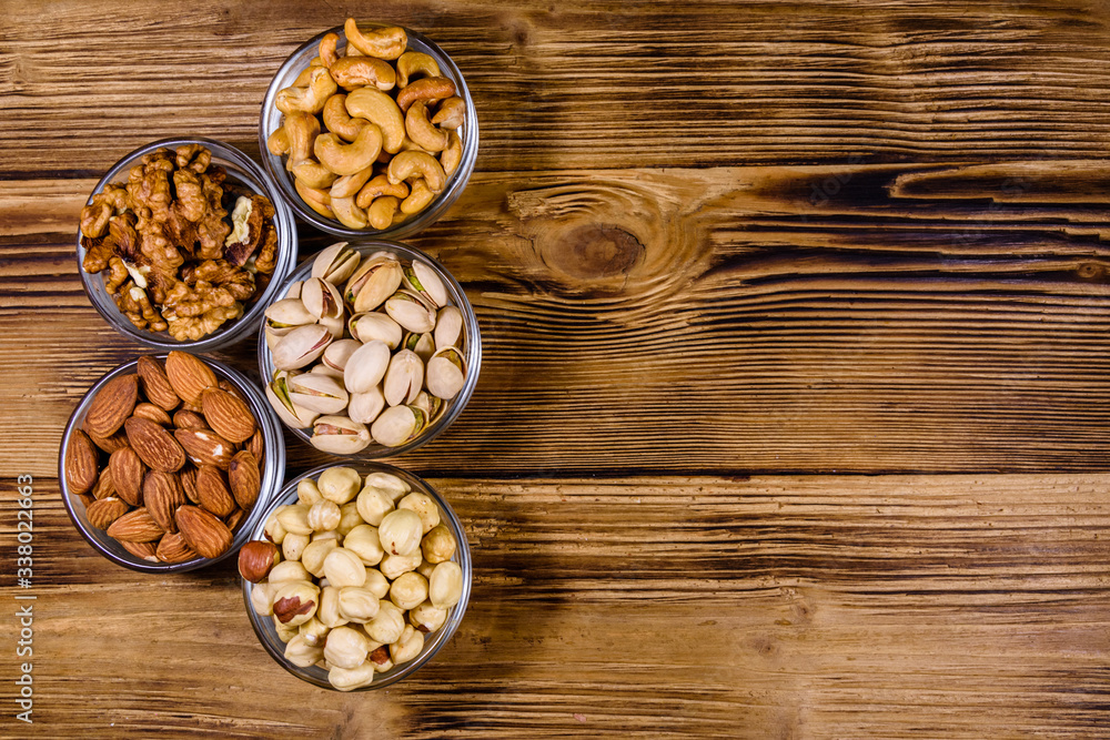 Various nuts (almond, cashew, hazelnut, pistachio, walnut) in glass bowls on a wooden table. Vegetarian meal. Healthy eating concept. Top view