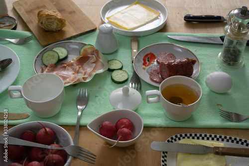 Fresh green cucumbers, radishes, croissant, sausage, bacon and cheese on a table set photo