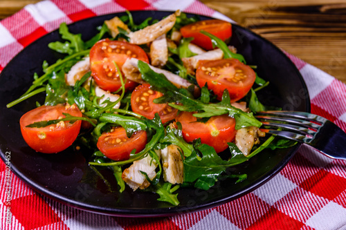 Roasted chicken breasts and salad with arugula and cherry tomatoes in a black plate