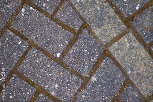 Weathered grey patio slabs in herringbone pattern with moss between blocks