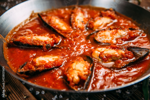 Closeup view on appetizing mussels in tomato sauce in a pan, horizontal format