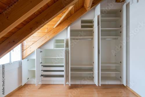 interior view of a custom-made closet with open doors built into a master bedroom with a sloping roof photo