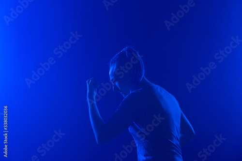Portrait of a man in with an unusual haircut mohawk iboxing in blue darkness background