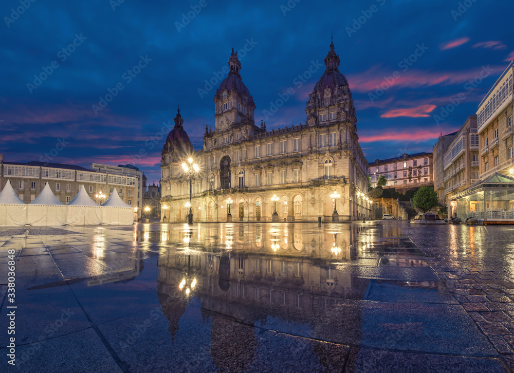 A Coruna, Spain. View of Praza de Maria Pita square with building of City Hall reflecting in puddle at dusk