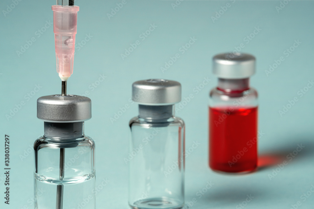 Three medical vial with liquid. A syringe with a needle is inserted into one medical vial. One medical vial with red liquid. Three medical vial with liquid. A syringe with a needle is inserted into one medical vial. One medical vial with red liquid.