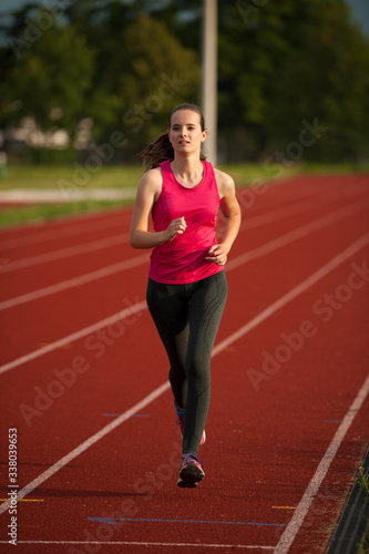 Beautiful young woman runner run on a track in early summer afternoon